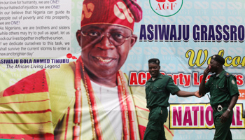 Environmental officials walk past a poster of former Lagos State Governor Bola Tinubu during the convention for the then newly formed All Progressive Congress (APC) party, Lagos, Nigeria, April 18, 2013 (Sunday Alamba/AP/Shutterstock)