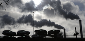 Smoke rises from a factory as a truck loaded with cars crosses a bridge in Paris (Michel Euler/AP/Shutterstock)