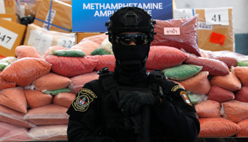 A Thai police officer guarding bags of confiscated methamphetamine pills (Chaiwat Subprasom/SOPA Images/Shutterstock)