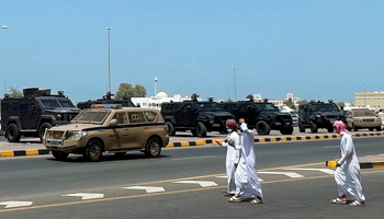 People pass by riot police cars in Sohar, Oman, May 25 (Uncredited/AP/Shutterstock)