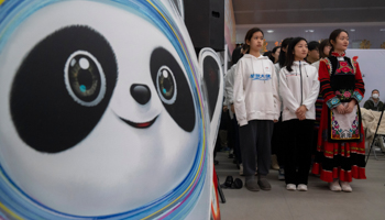 An image of Bing Dwen Dwen, mascot of the 2022 Winter Olympics, stands near students participants at a display of the Olympic flame in Beijing, December 9 (Mark Schiefelbein/AP/Shutterstock)