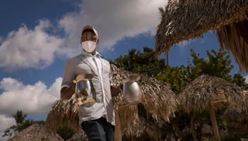 A masked hotel employee offers jugs of water to guests at Bayahibe beach, Dominican Republic, January 2021 (Orlando Barria/EPA-EFE/Shutterstock)