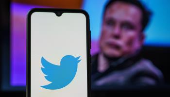 Twitter logo on smartphone and Elon Musk in the background (Shutterstock)