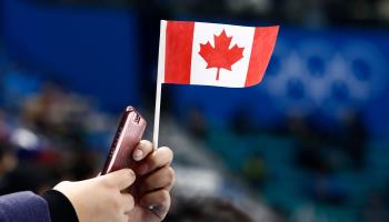 A spectator holds a Canadian flag and a phone at the Winter Olympics, 2018 (Larry W Smith/EPA-EFE/Shutterstock)