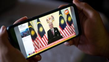 A man watches, on his mobile phone, the televised speech in which Prime Minister Ismail Sabri Yaakob announced the dissolution of parliament to pave the way for a general election (Xinhua/Shutterstock)