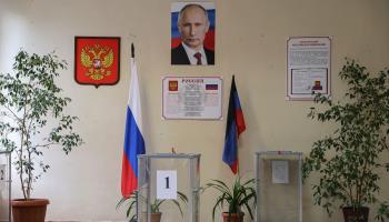 The coat of arms of Russia and a portrait of the Russian president are seen on a wall behind a ballot box during the local elections in Donetsk, Russian-occupied Ukraine in September 2023 (Stringer/EPA-EFE/Shutterstock)