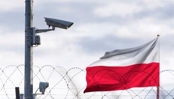 A Polish flag behind a barbed wire fence and surveillance camera (Shutterstock)