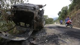 Motorcyclists pass a destroyed car used by members of the EMC. Cauca, March 19, 2024 (Ernesto Guzman/EPA-EFE/Shutterstock)