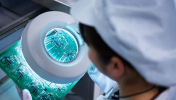 Worker at small parts manufacturing factory in China looking through magnifier at microchips (Mick Rya/Getty Images)